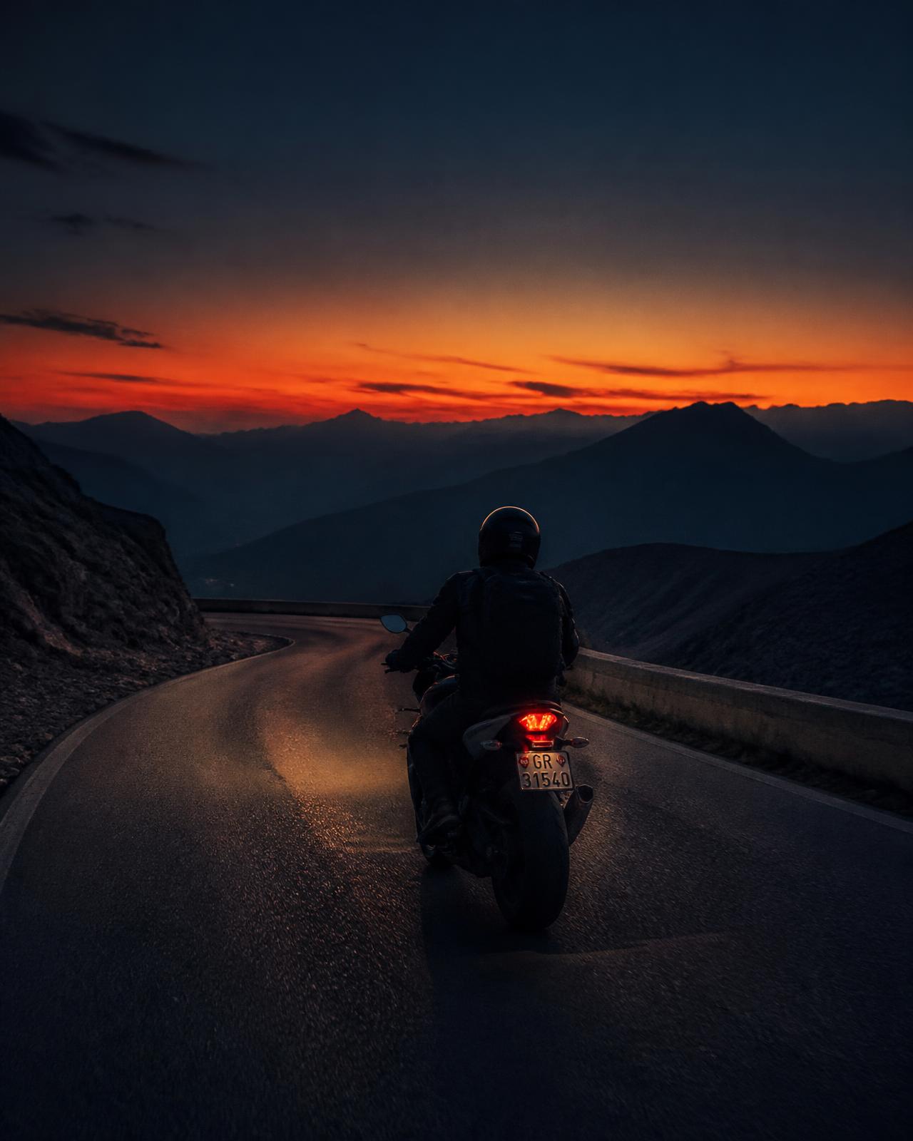 Motard de dos sur une route de montagne au coucher du soleil